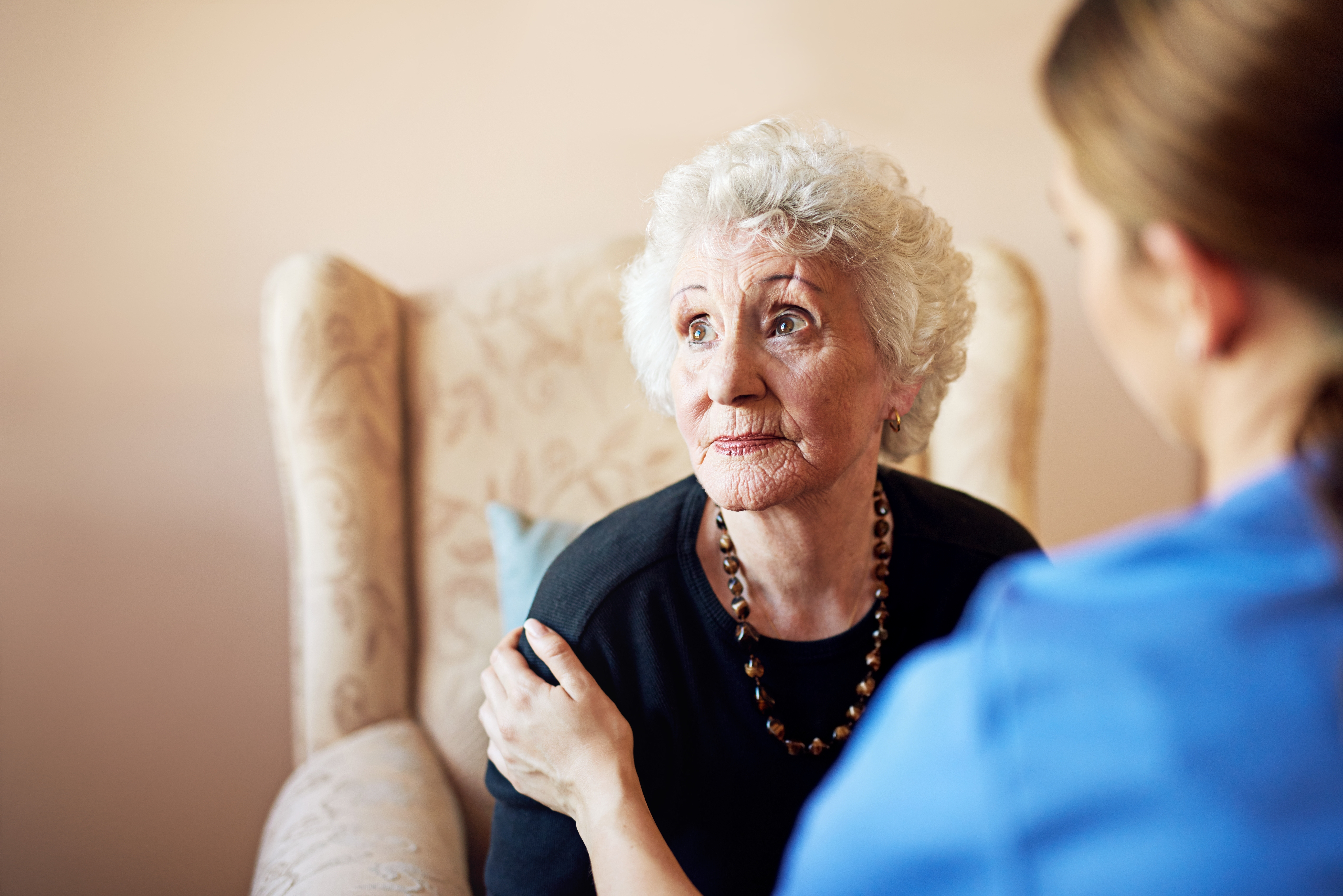 Elderly woman showing signs of financial abuse in a nursing home, looking worried while reviewing her finances.